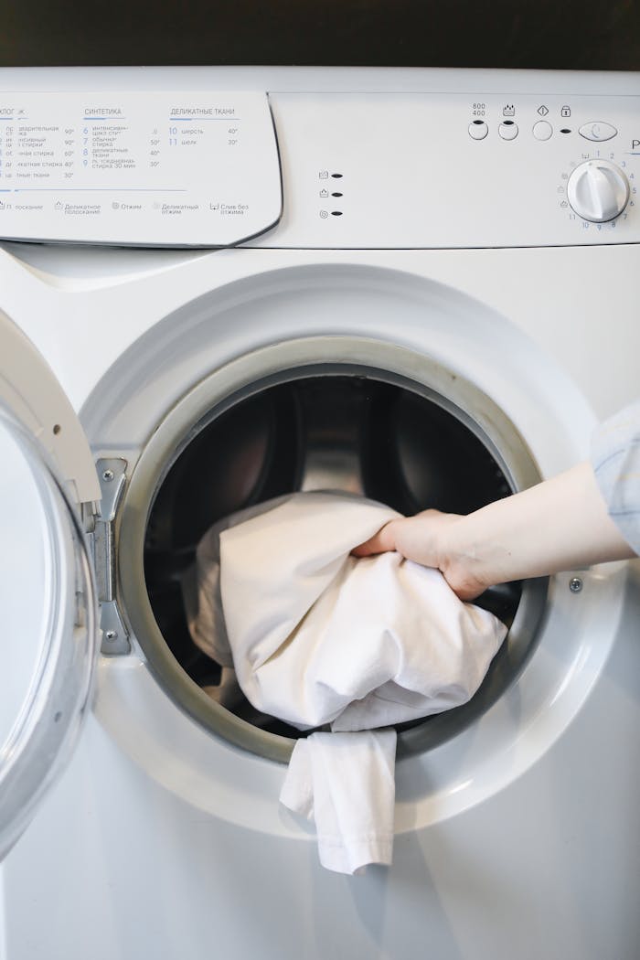 brand-01 Close-up of a persons hand putting laundry into a front-loading washing machine.