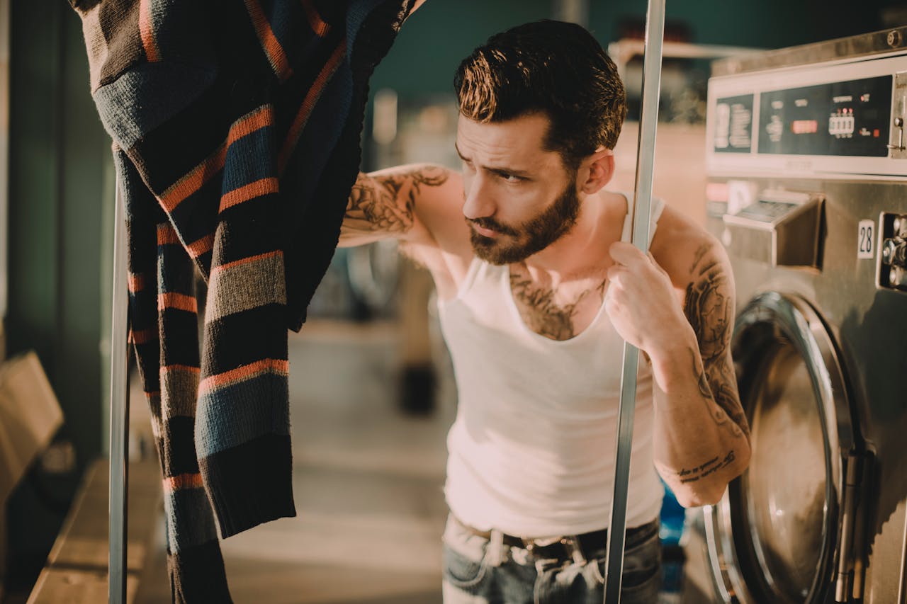 creative-01 Bearded man with tattoos using dryer in laundromat wearing tank top.