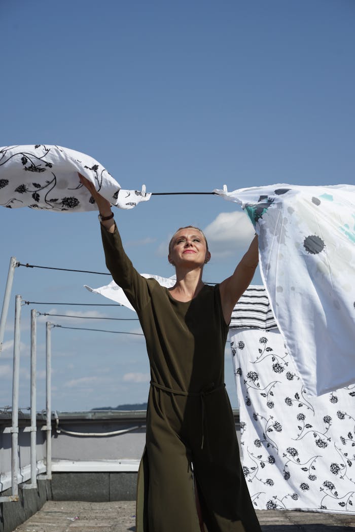 brand-02 A woman hangs laundry on a rooftop clothesline under a clear blue sky, enjoying a sunny day.